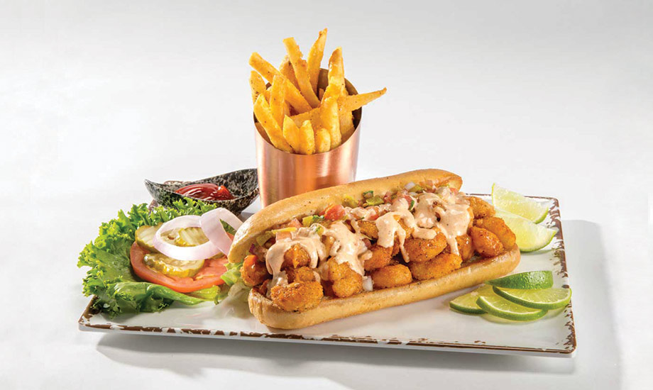 Image of shrimp po'boy sandwich served with fries and lettuce, tomato, onion and pickle on the side