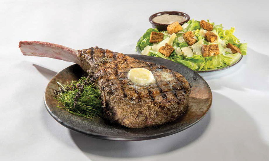 Image shows Tomahawk Ribeye steak with bone, served with Caesar salad