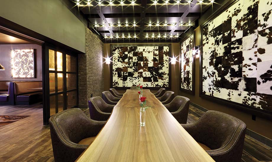 Image of the long group table in the Garrison Oak Steakhouse. The table looks like a solid piece of a tree cut long and the walls are decorated in real cowhide