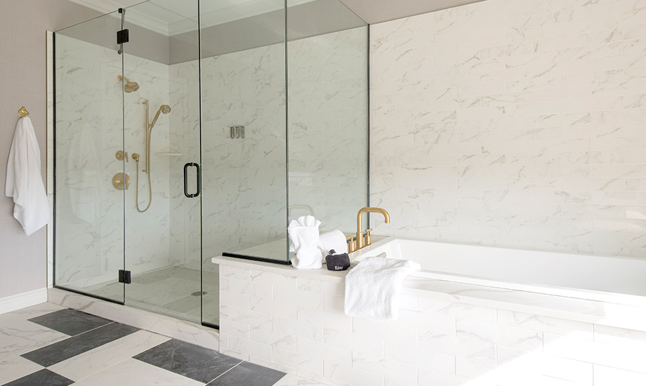Image of the shower and bathtub in the presidential suite, everything is white marble and the shower is large with static and detachable showers heads and a seat.