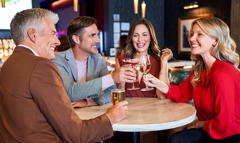 Image of 4 people smiling around a table raising a toast with various alcoholic beverages