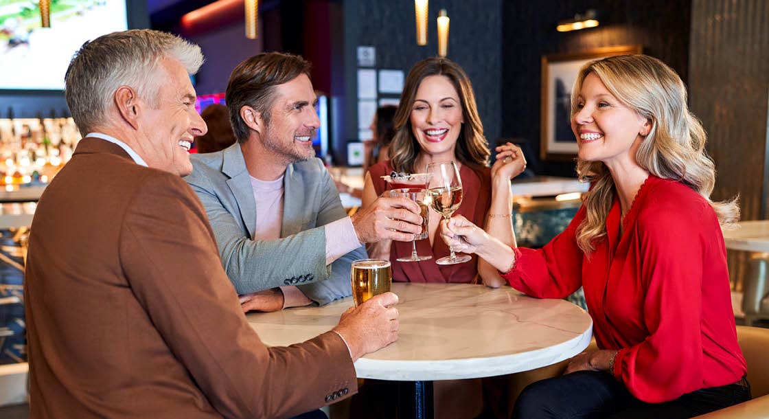 Image of two women and two men raising a toast at a table with various alcoholic beverages