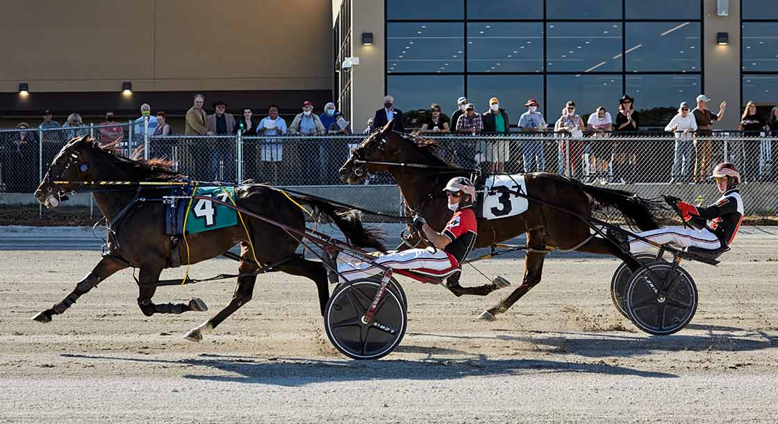 Two horses and their drivers pass by crowd at Oak Grove Racing, Gaming and Hotel Grandstand during harness race
