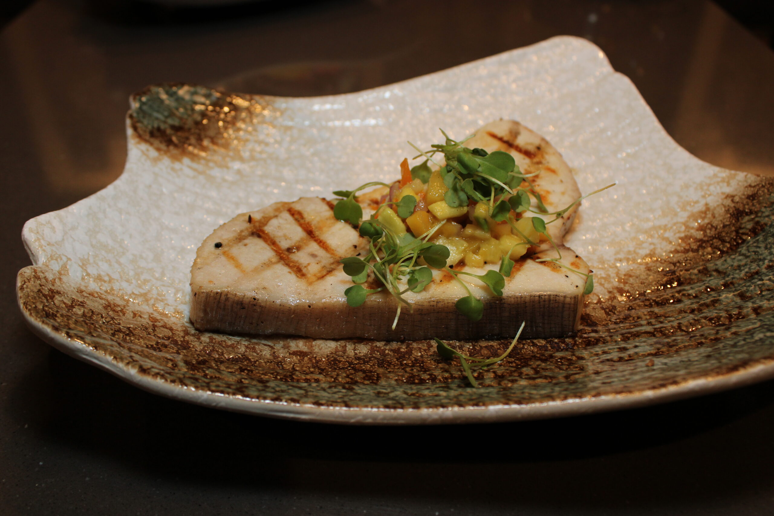 A plated swordfish steak topped with tropical pineapple and mango salsa