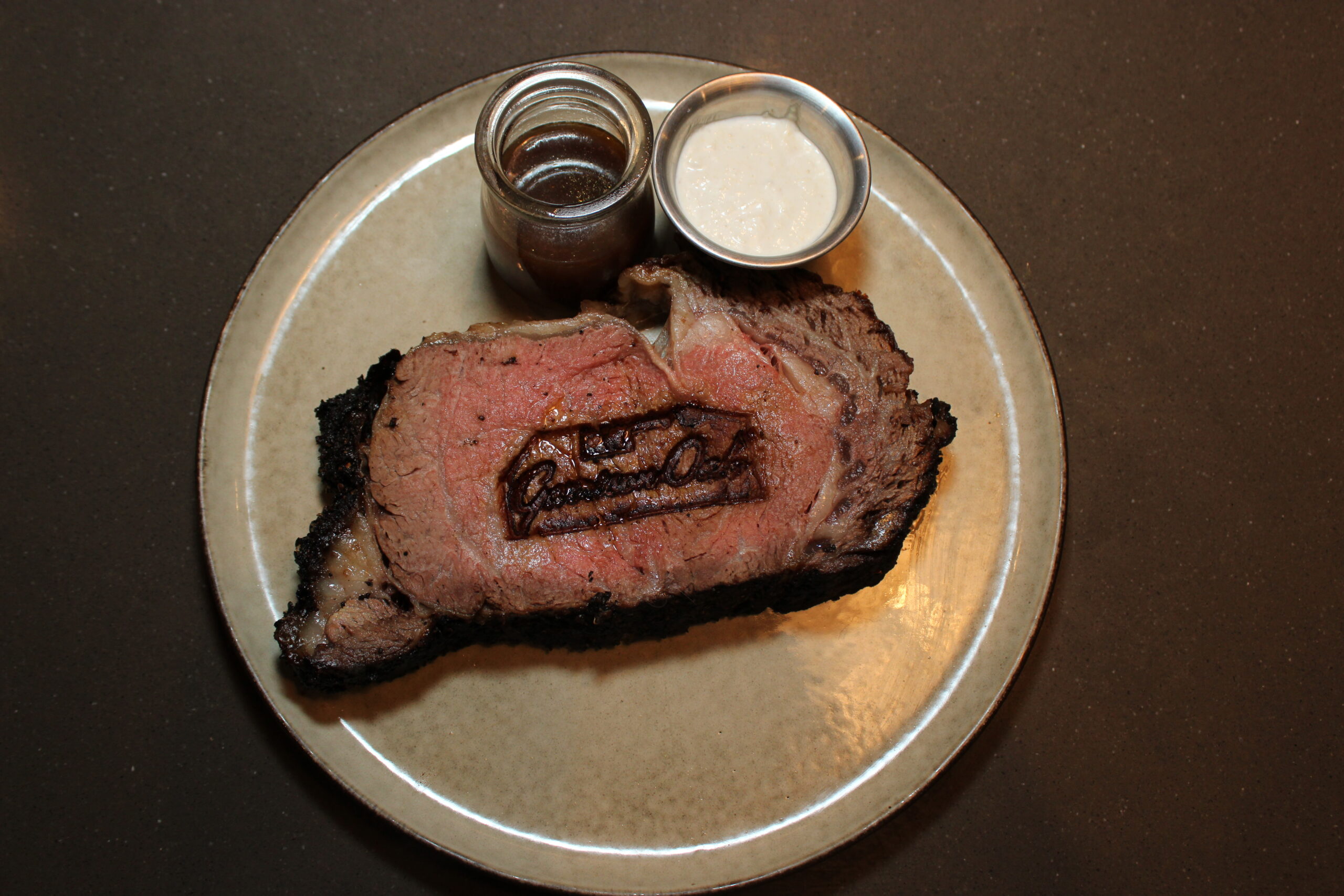 Image of King Cut Prime Rib with Au Jus and Horseradish Cream. The meat is branded with the "Garrison Oak" wordmark