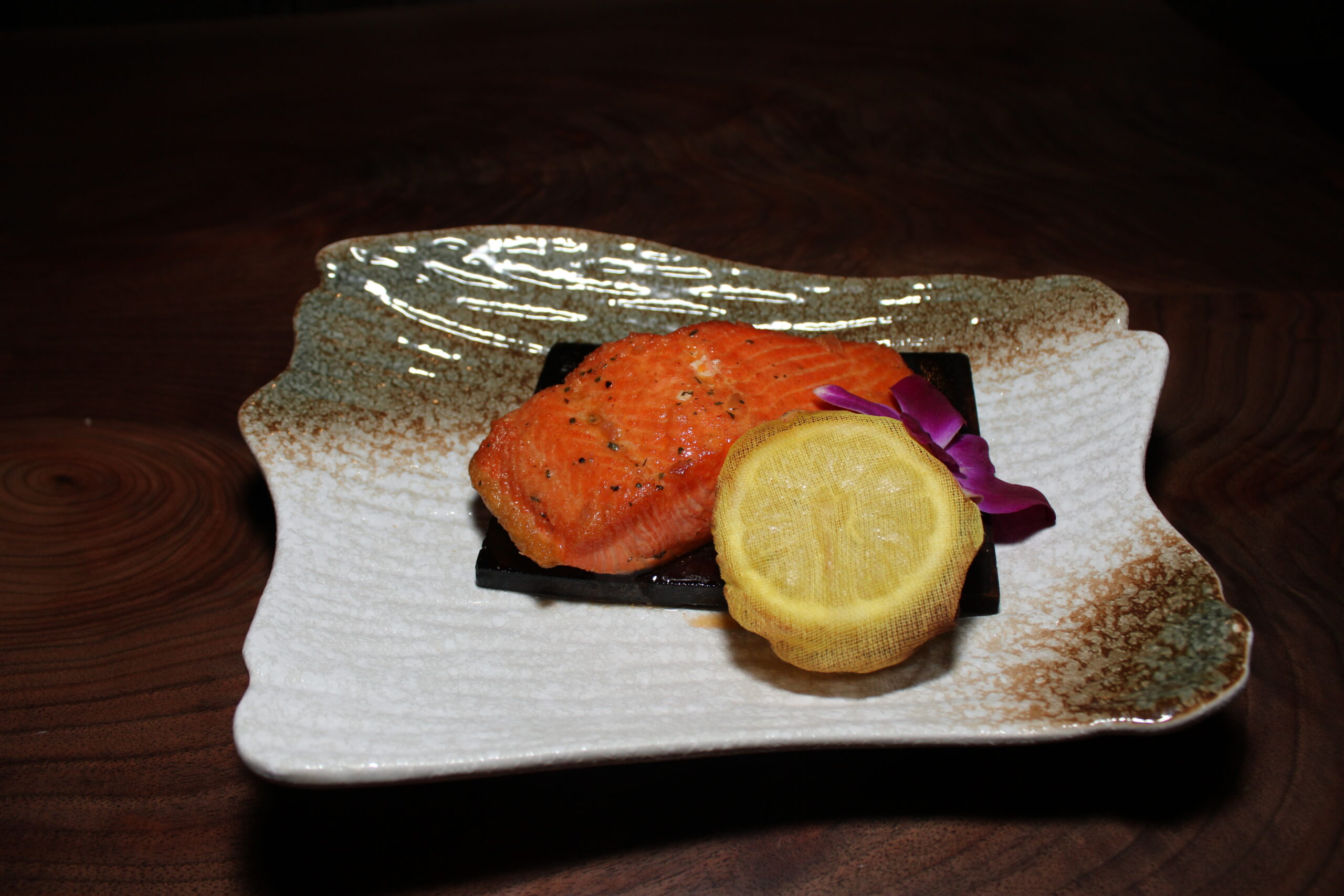 Image of a plated salmon filet on a wood plank with half a lemon